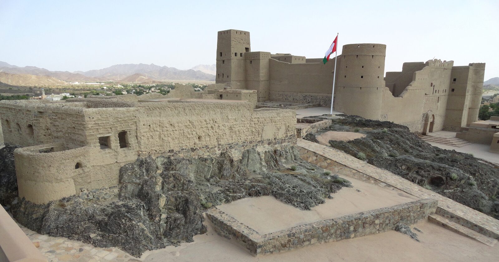 Wide view of Bahla Fort's mud-brick walls and towers rising against a clear sky in Oman
