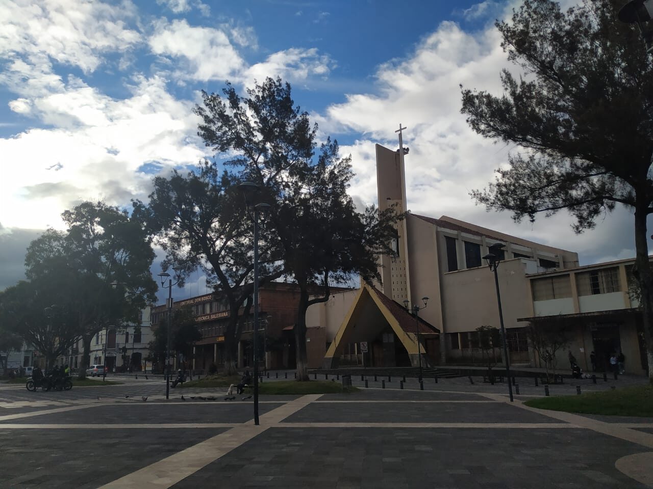 Diagonal exterior view of the María Auxiliadora church and its plaza in Cuenca, Ecuador, under a blue sky.