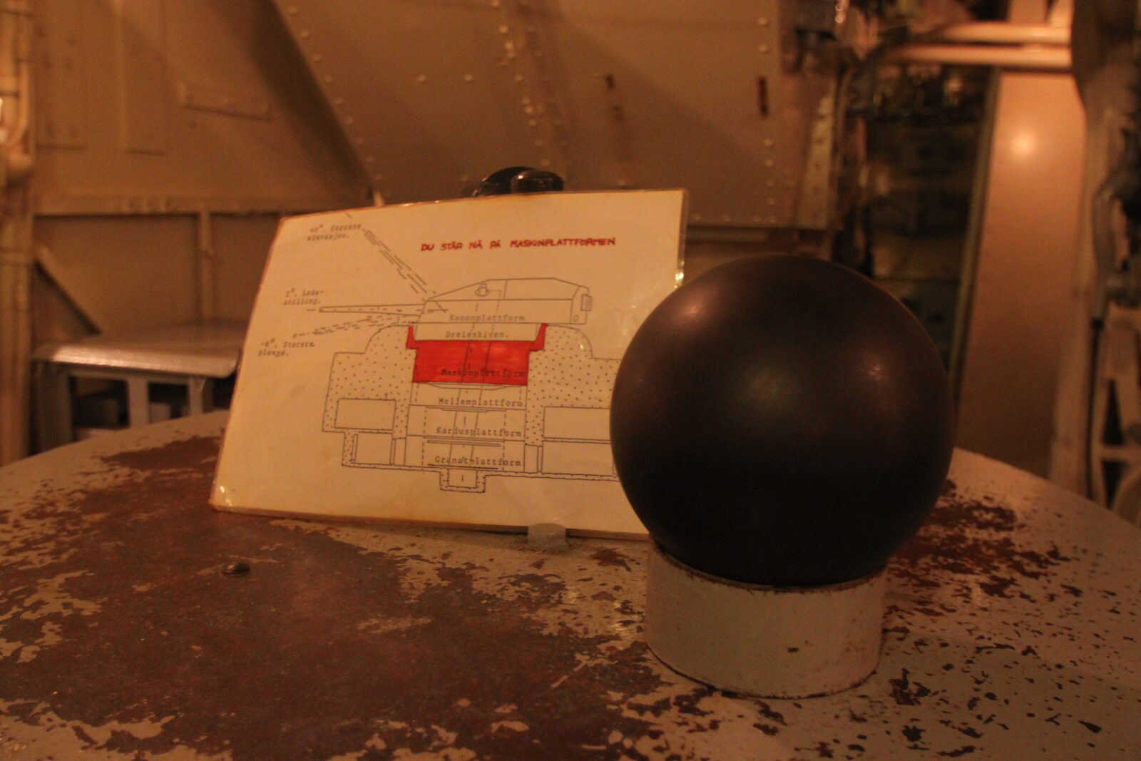 A large polished steel ball bearing sphere, roughly the size of a grapefruit, resting in the hand-worn mechanism of a gun turret race ring