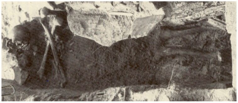 Excavated skeleton in a stone-lined grave with the skull placed above two long bones crossed in an X, forming a skull-and-crossbones pattern