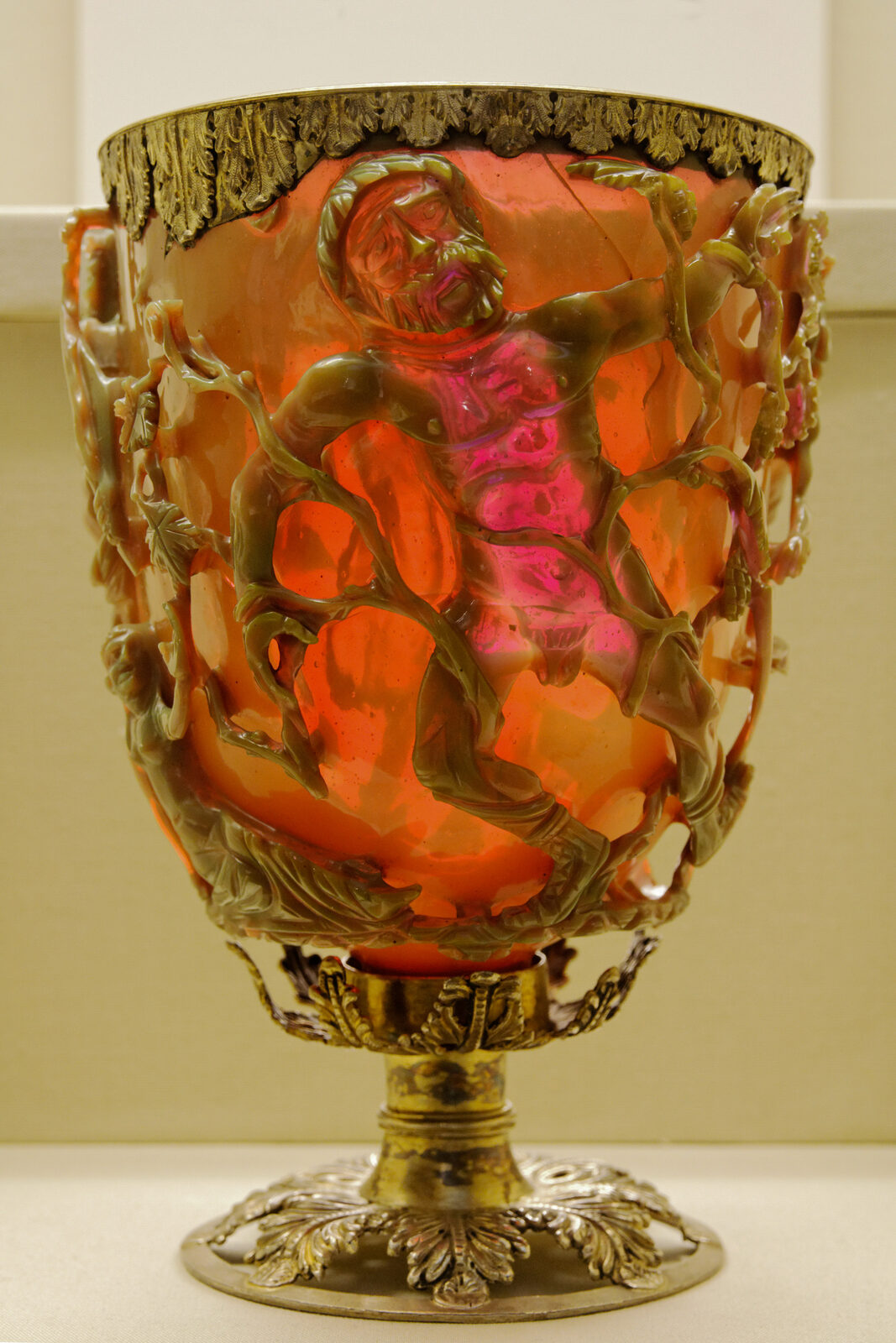 A Roman cage cup glowing translucent ruby red under transmitted light, its openwork frieze showing figures entangled in vines