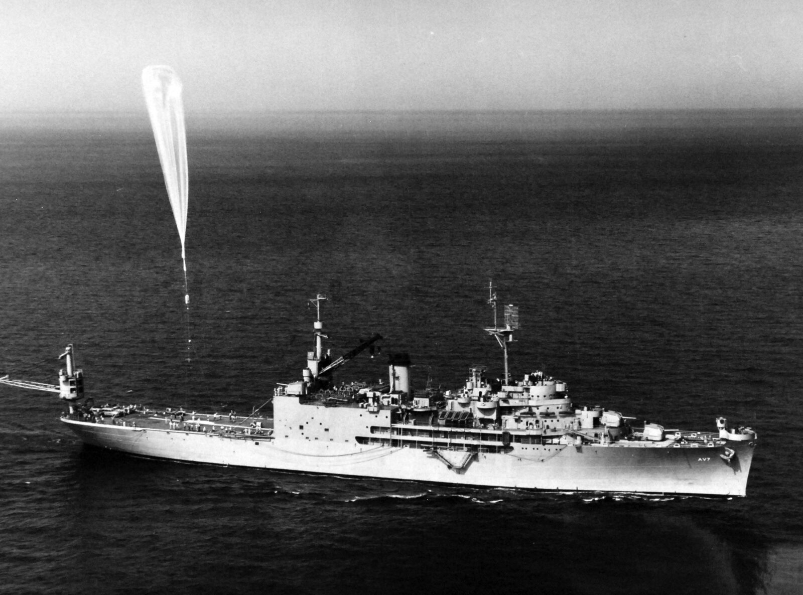 A large Skyhook high-altitude balloon inflating on the deck of the U.S. Navy seaplane tender USS Currituck as handlers remove its cover
