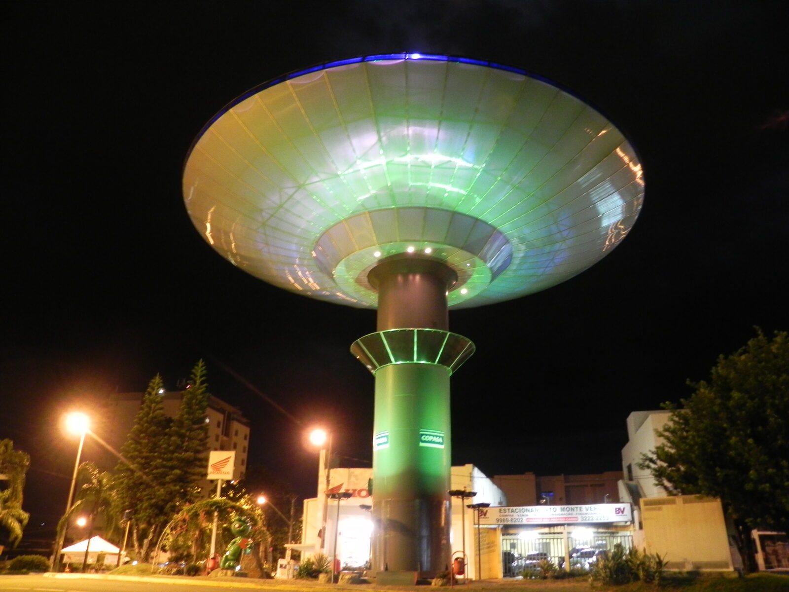 Disc-shaped Varginha water tower illuminated purple against the night sky